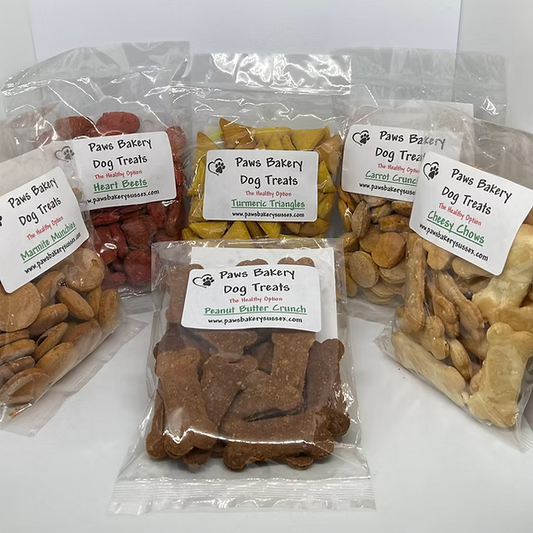 Assorted dog treats in clear packaging with 'Paws Bakery' labels on a white background